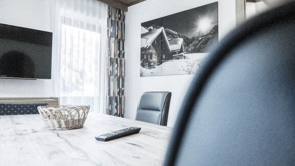 A modern living room with a large table and comfortable chairs. On the wall hangs a picture of a winter landscape. - Gästeheim Schmiedhof - Sölden