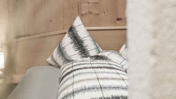 A cozy bedroom with a bed and pillows in a modern Scandinavian style. The walls are made of wood, creating a warm atmosphere. - Gästeheim Schmiedhof - Sölden