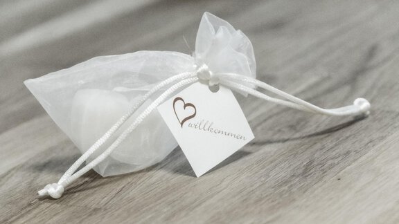 A small, transparent pouch with a heart-shaped tag. It is placed on a wooden surface. - Gästeheim Schmiedhof - Sölden