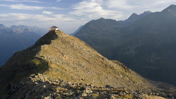 An impressive mountain peak with rocky terrain and gentle shadows. In the background, majestic mountains stretch under a cloudy sky. - Gstrein Andreas - Sölden
