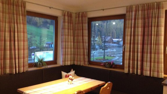 A cozy dining area with a wooden table and benches. The large windows offer a view of the green landscape outside. - Haus Almrausch - Sölden