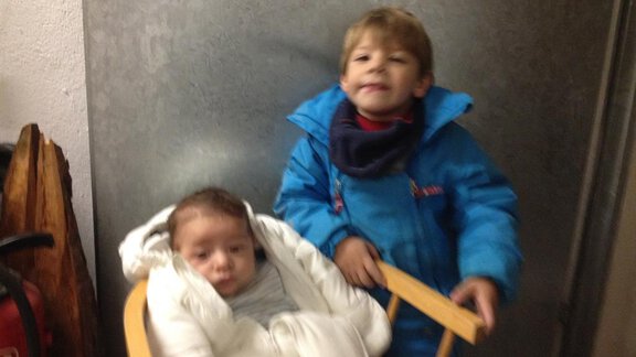 Two children in a room. A boy stands proudly next to a toddler in a carrier. - Haus Almrausch - Sölden
