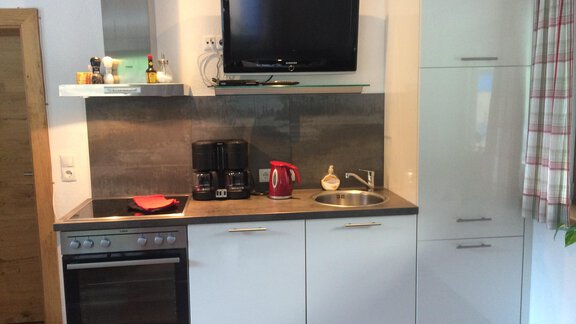 A modern kitchen with white cabinets and stainless steel appliances. On the countertop, there is a coffee maker and a kettle. - Haus Almrausch - Sölden
