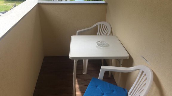 A small balcony with a white table and two chairs. An ashtray sits on the table, and the surroundings are green and peaceful. - Haus Almrausch - Sölden