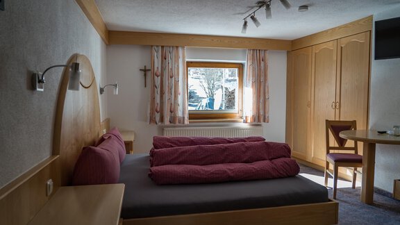 A cozy bedroom with a large bed and purple pillows. The room has wooden floors and a large window front that lets in daylight. - Haus Almrausch - Sölden