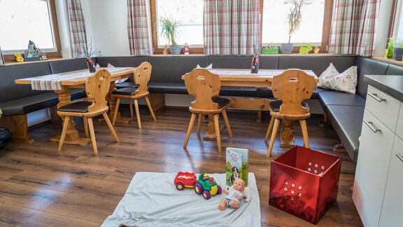 A cozy dining area with wooden furniture and colorful toys on the floor. Large windows provide plenty of daylight. - Haus Almrausch - Sölden