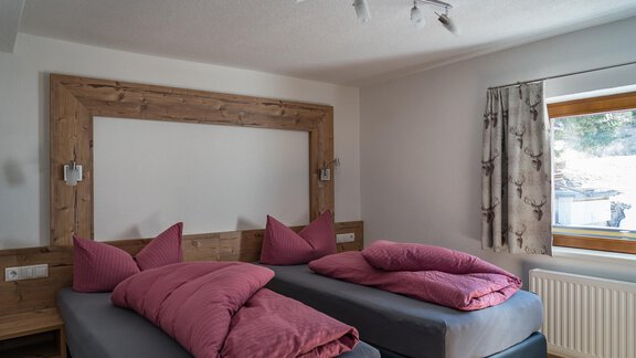 A modern bedroom with two beds and purple shell cushions. The room has a large window and a cozy wooden paneling. - Haus Almrausch - Sölden