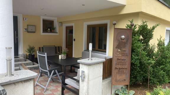 An inviting entrance area of a house with a terrace and modern furniture. Surrounded by small trees and flowers, the space creates a cozy atmosphere. - Haus Almrausch - Sölden