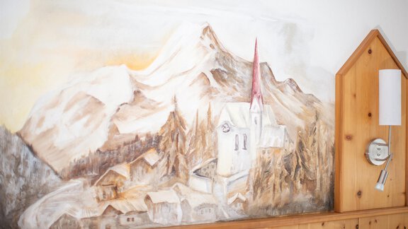 A mural featuring mountains and a church in a picturesque village. The warm color palette conveys a cozy atmosphere. - Haus Alpenstern - Sölden