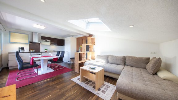 A modern living room with a cozy sofa and a dining table. The room has bright walls and large windows that let in plenty of light. - Haus Alpenstern - Sölden