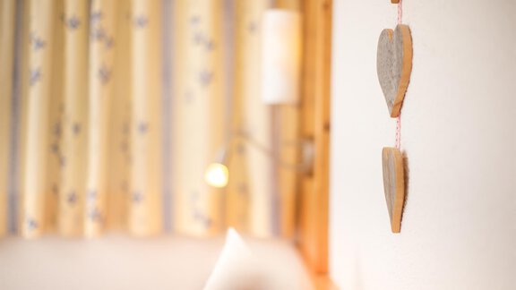 A cozy room with a wooden heart on the wall and soft curtains. The light is warm and inviting. - Haus Alpenstern - Sölden