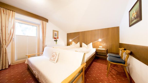 A cozy bedroom with two beds and wooden furniture. The windows are dressed with curtains, and there is a small table as well as a chair. - Haus Christian - Sölden