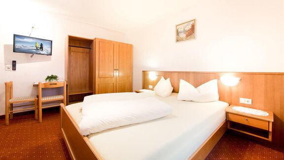 A cozy room with a double bed and a television. There is a small table and a wooden wardrobe. - Haus Christian - Sölden