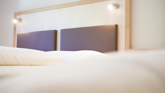 A comfortable bed with a wooden headboard and soft lights. The white bed linen creates an inviting atmosphere. - Haus Christian - Sölden