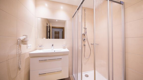 A modern bathroom with a shower cabin and a white sink. The walls are brightly tiled, and there is ample lighting. - Haus Christian - Sölden