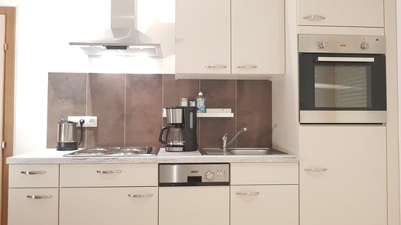 A modern kitchen with white cabinets and stainless steel appliances. It is well-organized and features a dishwasher, a sink, and a modern stove. - Haus Christian - Sölden