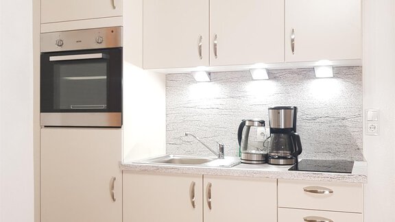 A modern kitchen with light cabinets and a built-in oven. On the countertop, there is a coffee machine and a sink. - Haus Christian - Sölden