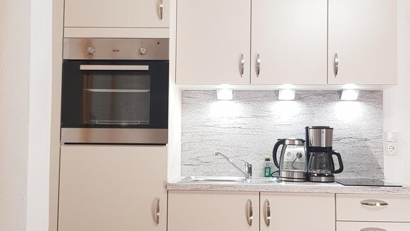 A modern kitchen with bright cabinets and a stone countertop. It is equipped with an oven, a coffee machine, and integrated lighting. - Haus Christian - Sölden