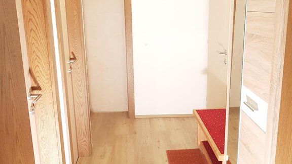 A bright hallway with wooden French doors and a large mirror. The floor is made of wood, and a red carpet lies in front of a bench. - Haus Christian - Sölden