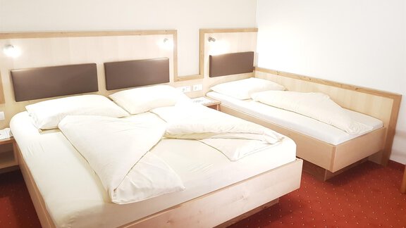 A modern bedroom with two beds and light bedding. The floor is covered with a red carpet. - Haus Christian - Sölden