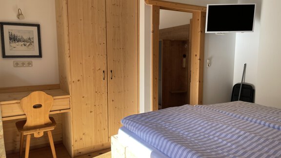 A cozy bedroom with a wooden wardrobe and a desk. There is a bed with striped bedding and a television on the wall. - HAUS ERIKA apartments - Sölden