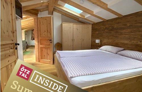 A cozy bedroom with a large bed and wooden paneling. In the foreground lies a map for leisure activities in the summer. - HAUS ERIKA apartments - Sölden