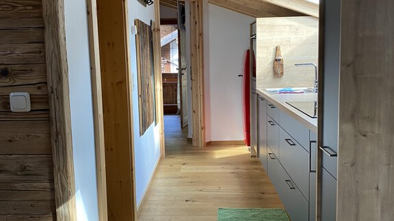 A bright hallway with wooden ceilings and a modern kitchen unit. The floor is made of wood and a green carpet lies in the center. - HAUS ERIKA apartments - Sölden