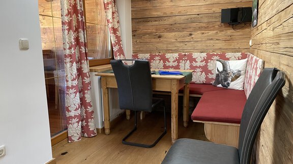 A cozy dining area with wood paneling and floral curtains. The table is equipped with a chair and a bench. - HAUS ERIKA apartments - Sölden