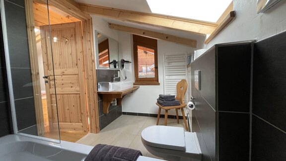 A modern bathroom with wood and tile elements. There is a bathtub, a sink, and a window view. - HAUS ERIKA apartments - Sölden