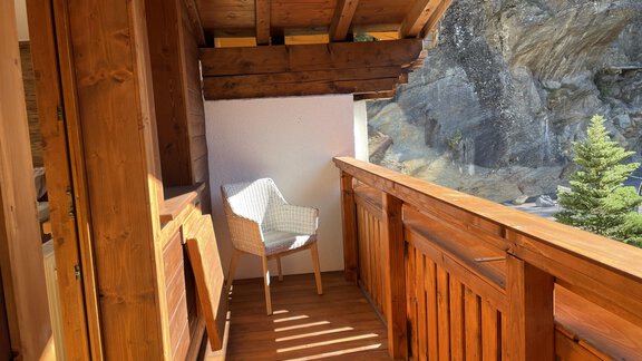 A wooden balcony with a cozy white chair and a view of rocks and trees. The interplay of light and shadow creates an inviting atmosphere. - HAUS ERIKA apartments - Sölden