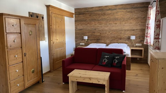 A cozy room with wood paneling, a red sofa, and a small table. There are two beds as well as a wooden wardrobe. - HAUS ERIKA apartments - Sölden
