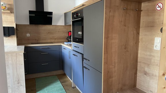 A modern kitchen with gray cabinets and wood details. It is equipped with a stove, oven, and sink. - HAUS ERIKA apartments - Sölden