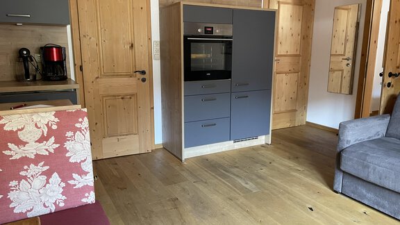 A modern kitchen with a wooden floor and light walls. In the foreground, there is a gray kitchen island and a cozy seating area. - HAUS ERIKA apartments - Sölden