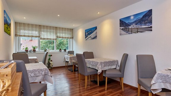 A bright room with elegant tables and chairs. Pictures of landscapes hang on the walls. - Haus Fontana - Sölden