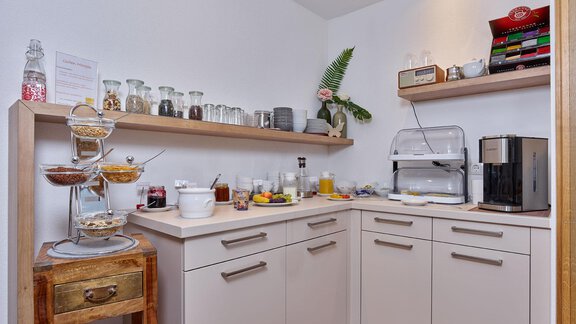 A modern kitchenette with open shelves that hold dishes and food. On the table are various breakfast offerings and a coffee machine. - Haus Fontana - Sölden
