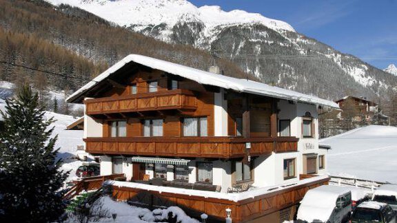 A beautiful house in the snow with wooden cladding and several balconies. In the background, snow-covered mountains can be seen. - Haus Fridolin - Sölden