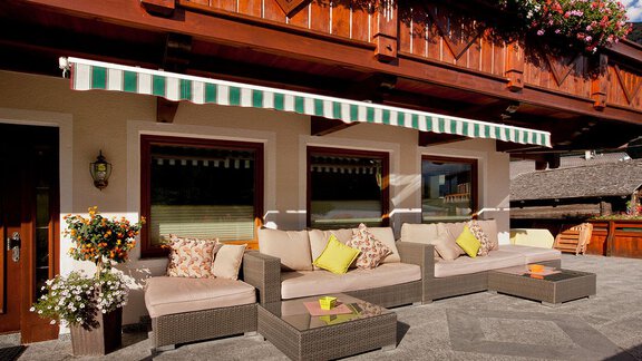 A cozy terrace with a gray sofa set and colorful cushions. Above the terrace hangs an awning fabric in green and white stripes. - Haus Fridolin - Sölden