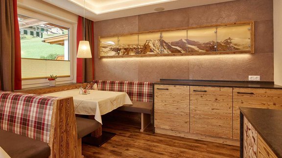A cozy room with wooden paneling and a bright dining area. On the wall, there is a mural of mountains, highlighting the alpine atmosphere. - Haus Fridolin - Sölden