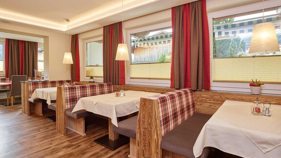 A cozy restaurant with wooden interior and upholstered benches. The atmosphere is inviting and friendly, with warm lighting and large windows. - Haus Fridolin - Sölden
