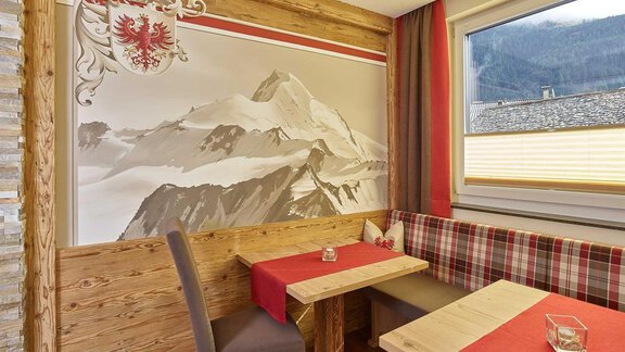 A cozy dining room with wooden paneling and red-and-white checkered tablecloths. On the wall, there is a large picture of a snow-covered mountain. - Haus Fridolin - Sölden