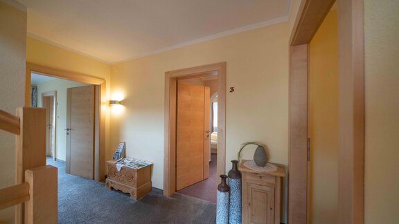 A bright hallway with warm wall colors and wooden details. On the left, there are two rooms and a table with decoration visible. - Haus Fridolin - Sölden