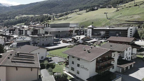 A picturesque mountain landscape with modern buildings and beautiful green spaces. In the background, the mountains are visible under a blue sky. - Haus Gabriela - Sölden