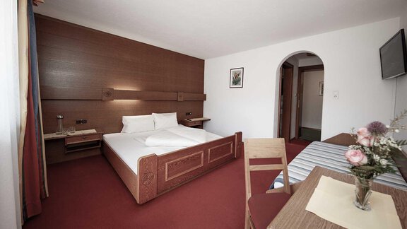 A cozy hotel room with a large bed and a small table. The decor is simple and invites relaxation. - Haus Gabriela - Sölden