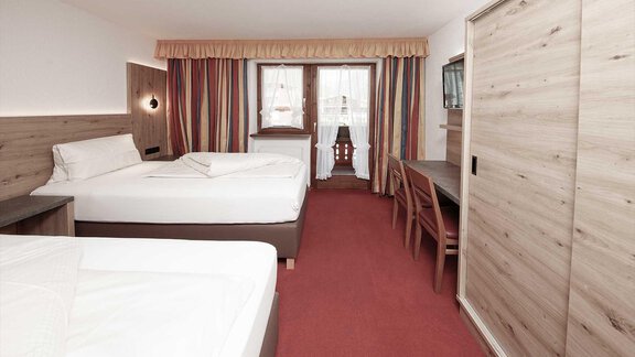 A modern hotel room with two beds and a desk. The decor is in warm wood tones and the windows let in plenty of light. - Haus Gabriela - Sölden