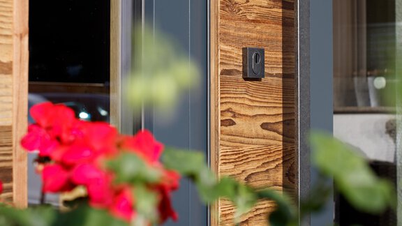 A modern wooden house with a beautiful wooden facade. In the foreground, red flowers are blooming. - Haus Gondelblick - Sölden