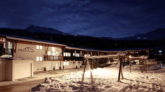 A cozy building in the snow at night. The surroundings are quiet, with gentle mountains in the background and a dark, cloudy sky. - Haus Ingrid - Sölden