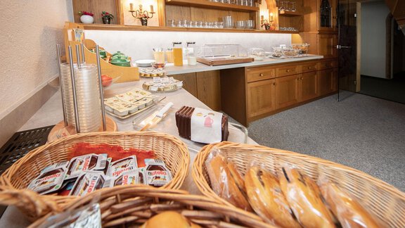 An inviting breakfast buffet with fresh rolls, jam, and various drinks. The wooden cabinet in the background displays a neat arrangement of dishes and glasses. - Haus Montjola - Sölden