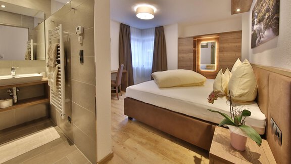 A modern hotel room with a large bed and wooden flooring. The bathroom is bright and well-equipped. - Haus Söldenblick - Sölden