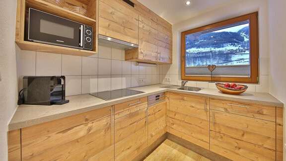 A modern kitchen with wood fronts and an elegant countertop. It features a large window view of the mountains and offers ample space for meal preparation. - Haus Söldenblick - Sölden