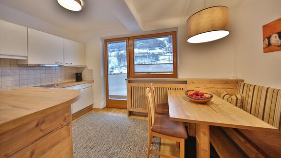 A cozy kitchenette with wooden shelves and a dining table. Large windows provide a view of the winter landscape. - Haus Söldenblick - Sölden